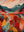 A vertical hand-painted textured oil painting featuring an abstract sunset landscape with bold red, orange, and blue impasto brushstrokes of mountains, displayed in a minimalist living room above a wooden table.