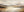 A large horizontal hand-painted modernist oil painting of a misty mountain range and calm lake in warm earth tones, displayed in a luxury minimalist living room.