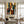 Handmade mid-century modern abstract oil painting featuring stylized people silhouettes in terracotta, mustard yellow, and emerald green with rich brush textures, hanging in a bright minimalist entryway above a dark wood console table next to a staircase.