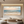 Large horizontal abstract oil painting of ocean waves with heavy impasto texture in blue and beige, displayed in a minimalist modern living room above a wooden coffee table.