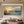 Large horizontal handmade oil painting of an abstract ocean sunset with golden sunlight reflecting on blue waves, styled in a minimalist living room with neutral-colored floor cushions and a wooden table.