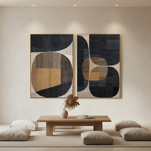 A pair of hand-painted abstract geometric oil paintings featuring bold black, earthy ochre, and tan shapes, styled above a neutral sofa in a modern boho-chic living room with warm wooden accents.