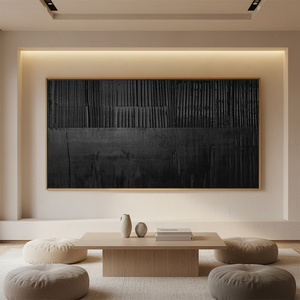 Large horizontal handmade black oil painting with heavy vertical textured ridges, displayed in a warm modern living room above a wooden coffee table with floor cushions.