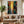 A 100% handmade abstract modern oil painting featuring vertical stripes of various colors, with a heavily textured, prominent metallic gold center stripe flanked by dark green, blue, and red brushstrokes.