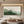 Hand-painted 3D abstract texture art with bold emerald green and white strokes, displayed in a bright modern living room with a grey sofa.