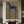 A hand-painted abstract folk oil painting of a slender blue horse with white symbols and a rider with a wide-brimmed hat, hung in a dark moody study room above a wooden console table with antique books.