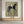 A large hand-painted abstract folk oil painting of a slender black horse and rider with a wide-brimmed hat on a textured olive green background, hung in a modern beige living room above a sofa.