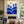100% hand-painted mid-century minimalist abstract landscape oil painting featuring geometric cobalt blue hills and trees under a warm yellow sun on a cream canvas background, styled as a premium vertical statement wall art piece in a modern minimal staircase gallery wall setting as visualized in Minimalist-Blue-Landscape-for-room-decor.jpg and Minimalist-Blue-Landscape-for-staircase-gallery-wall.jpg.
