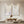 A pair of large hand-painted abstract paintings featuring black fluid lines on a beige and off-white textured background, styled in a modern sunlit minimalist living room above a wooden coffee table.