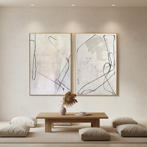 A pair of large hand-painted abstract paintings featuring black fluid lines on a beige and off-white textured background, styled in a modern sunlit minimalist living room above a wooden coffee table.