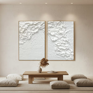 Set of two hand-painted white minimalist abstract paintings featuring heavy 3D impasto texture with wave-like patterns, displayed in a serene Zen-style living room setting.