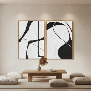 Set of two hand-painted Wabi-Sabi abstract oil paintings featuring bold, fluid black lines on a heavily textured off-white background, styled in a modern minimalist living room over a wooden table.