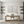 Pair of hand-painted white abstract paintings with heavy diagonal 3D impasto brushstrokes, shown in a modern minimalist living room featuring a wooden table and low seating.