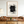 Hand-painted abstract black and white oil painting with textured charcoal lines and a bold central block, styled on a neutral wall above a boho wabi-sabi living room seating area.