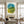 Large hand-painted abstract oil painting with translucent, overlapping watercolor-like shapes in shades of ocean blue, green, and mustard yellow, curated above a dark wood table in a boho minimalist living room.