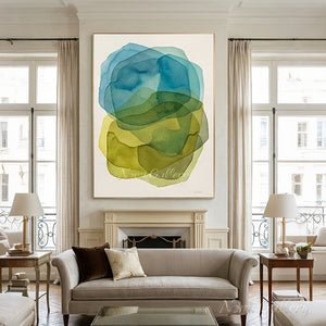 Large hand-painted abstract oil painting with translucent, overlapping watercolor-like shapes in shades of ocean blue, green, and mustard yellow, curated above a dark wood table in a boho minimalist living room.