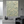 Handmade large 3D heavy textured abstract oil painting in calming sage green and cream tones with prominent palette knife strokes, hanging on a white minimalist gallery wall next to a modern staircase and a lounge armchair.