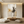 Original handmade Japandi style abstract oil painting featuring warm ochre washes and charcoal black brushstrokes resembling misty trees, displayed on a beige plaster wall in a modern minimalist living room above a low wooden coffee table with floor cushions.