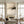 Handmade large minimalist abstract oil painting featuring warm beige and oatmeal tones with an expressive charcoal black sweep and fine vertical lines, styled in a warm Boho living room above a low dark wood table with floor pillows.