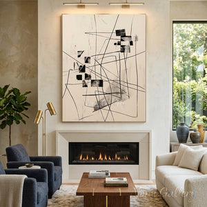Hand-painted abstract canvas painting featuring chaotic yet structured black lines and black geometric squares on a warm beige background, framed and hung on a minimalist home office wall above a wooden desk.