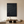 Large hand-painted 3D textured black abstract oil painting with two concentric swirl patterns, hanging in a modern minimalist living room with a black armchair.