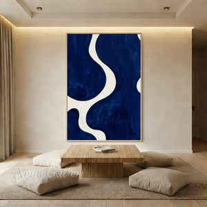Large handmade abstract oil painting featuring massive organic fluid shapes of deep navy blue divided by flowing ivory white paths, enclosed in a black frame on a minimalist gallery staircase wall above a modern white credenza.