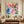 Hand-painted heavy texture abstract oil painting showing a colorful, dense cluster of blooming flowers in shades of peach pink, coral, yellow, and peacock blue with vertical paint drips.