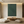 A hand-painted 3D textured oil painting in deep forest green, featuring a prominent vertical S-curve relief with fine rhythmic lines, displayed in a warm modern minimalist room.