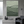 Large handmade minimalist abstract canvas painting featuring a soft sage green organic block and a sweeping, continuous fluid black curve on an ivory background, framed in black and hung on a modern warm-grey living room wall above a contemporary sofa.