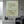 Handmade 3D textured oil painting featuring a swirling abstract green and cream flower, hanging on a concrete wall in a modern living room with a grey armchair.
