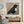 Hand-painted minimalist textured oil painting of a single black bird flying across a soft yellow sun on a warm oatmeal and sand colored canvas background.